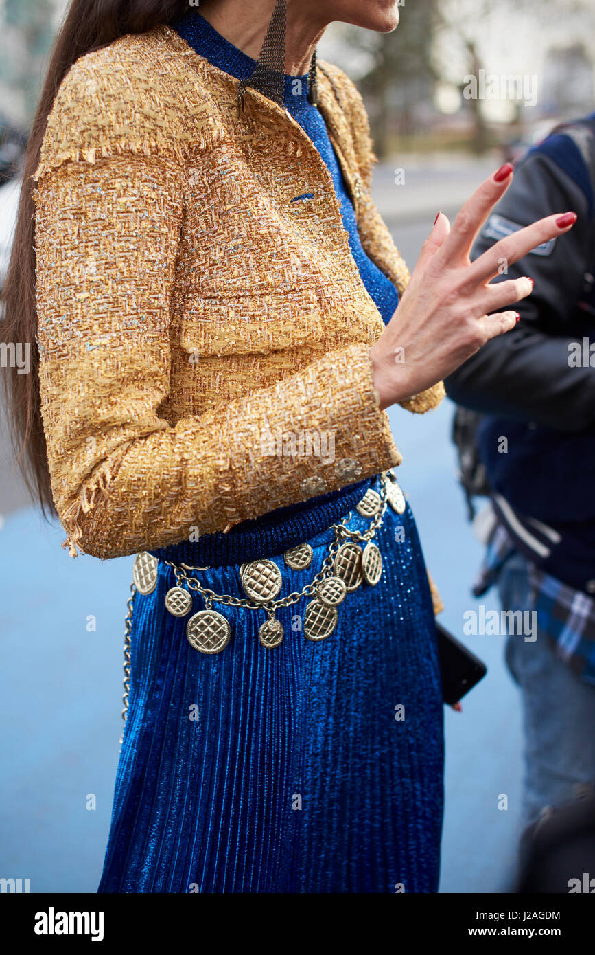 LONDON - FEBRUARY, 2017: Mid section of woman wearing a short jacket, blue pleated skirt and a Chanel medallion chain belt in the street during London Fashion Week, vertical, side view Stock Photo
