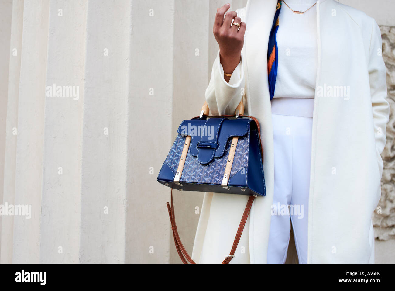 LONDON - FEBRUARY, 2017: Mid section of woman wearing white trousers, coat and metal Chopard belt holding a blue handbag in the street against a building during London Fashion Week, horizontal, front view Stock Photo