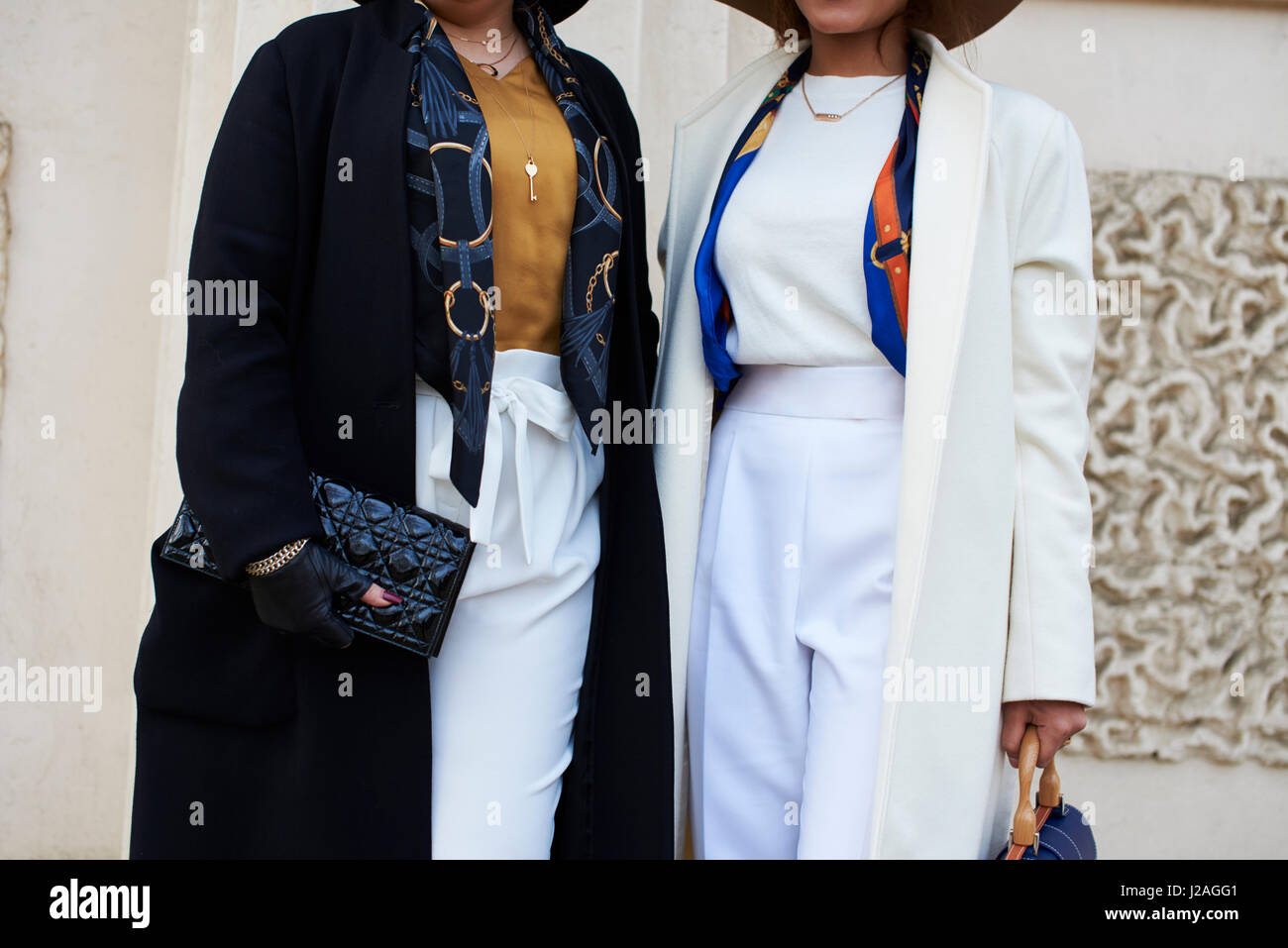 LONDON - FEBRUARY, 2017: Mid section of two women in the street holding handbags, a Chanel clutch bag on the left, while woman on the right wears a Chopard belt, during London Fashion Week, horizontal, front view Stock Photo