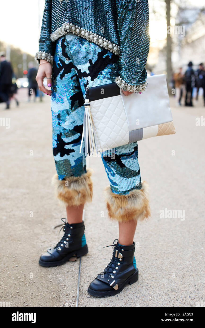LONDON - FEBRUARY, 2017: Low section of woman in Ashish trousers and top holding an oversized Chanel clutch handbag standing in the street during London Fashion Week, vertical, front view Stock Photo