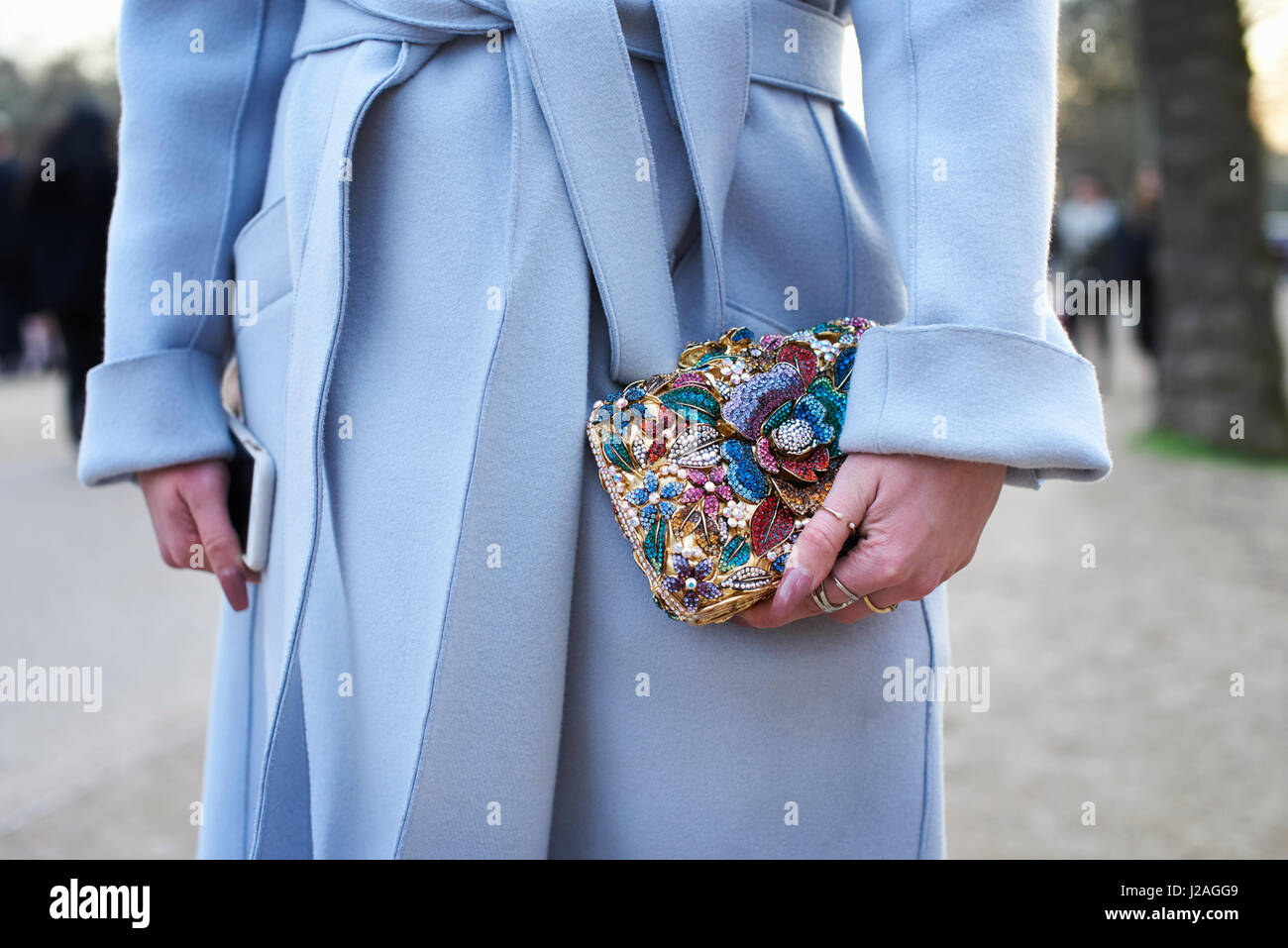 LONDON - FEBRUARY, 2017: Mid section of woman dressed in pale blue wool coat holding smartphone and small appliqué decorated purse in the street during London Fashion Week, horizontal, front view Stock Photo