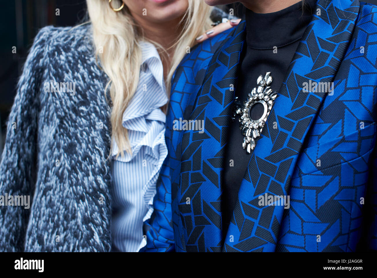LONDON - FEBRUARY, 2017: Mid section close up of two fashionable women, one wearing a wool jacket and the other a patterned silk jacket, London Fashion Week, horizontal, back view Stock Photo