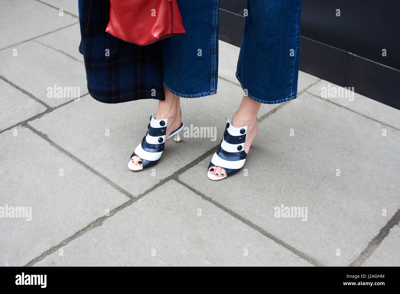 LONDON - FEBRUARY, 2017: Low section of woman wearing three quarter length jeans and  kitten heel striped leather open toe mules standing in the street during London Fashion Week, horizontal high angle close up Stock Photo
