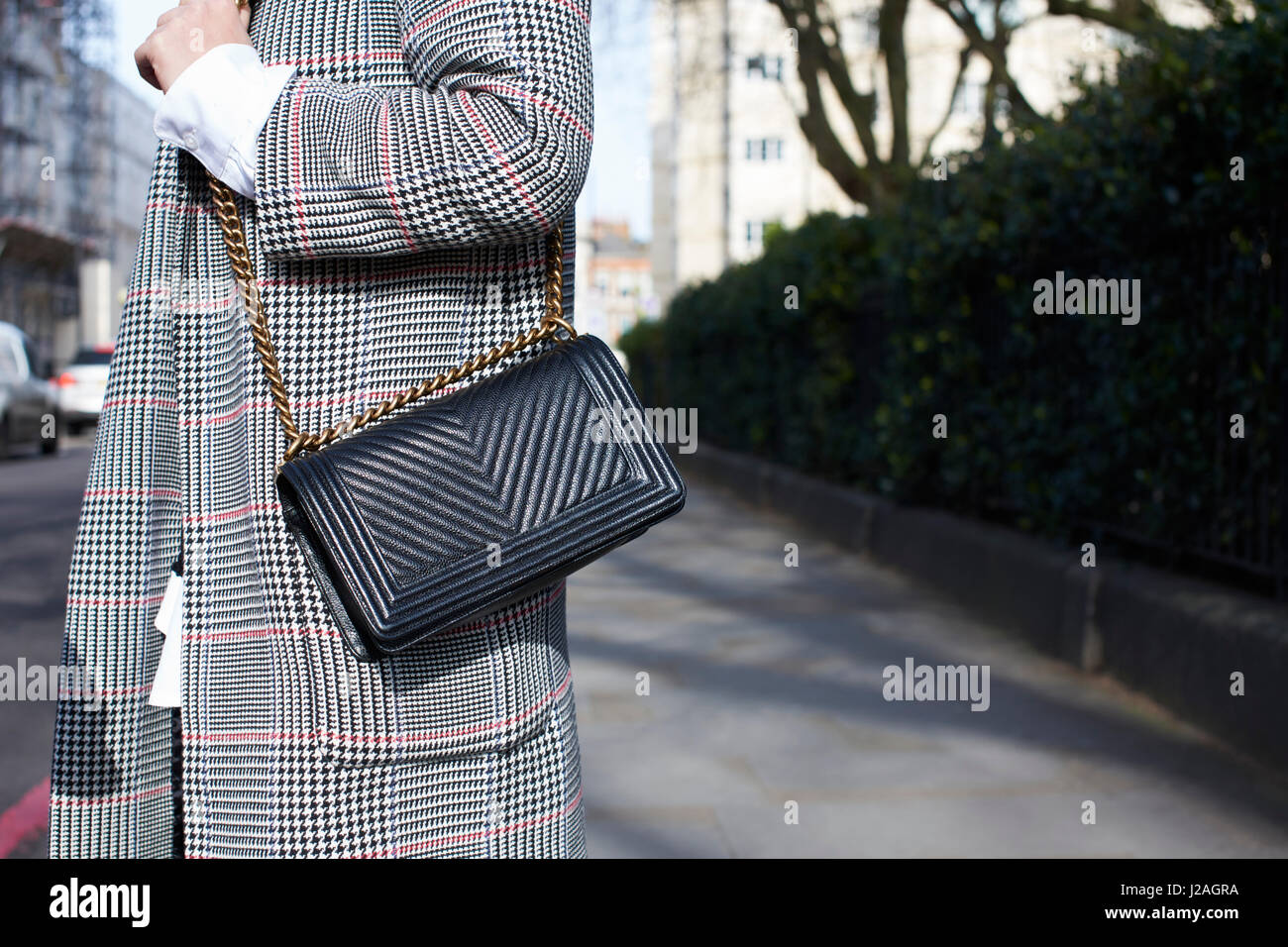 LONDON - FEBRUARY, 2017: Mid section of woman wearing Prince of Wales check coat and black Chanel cross body handbag standing in street during London Fashion Week Stock Photo