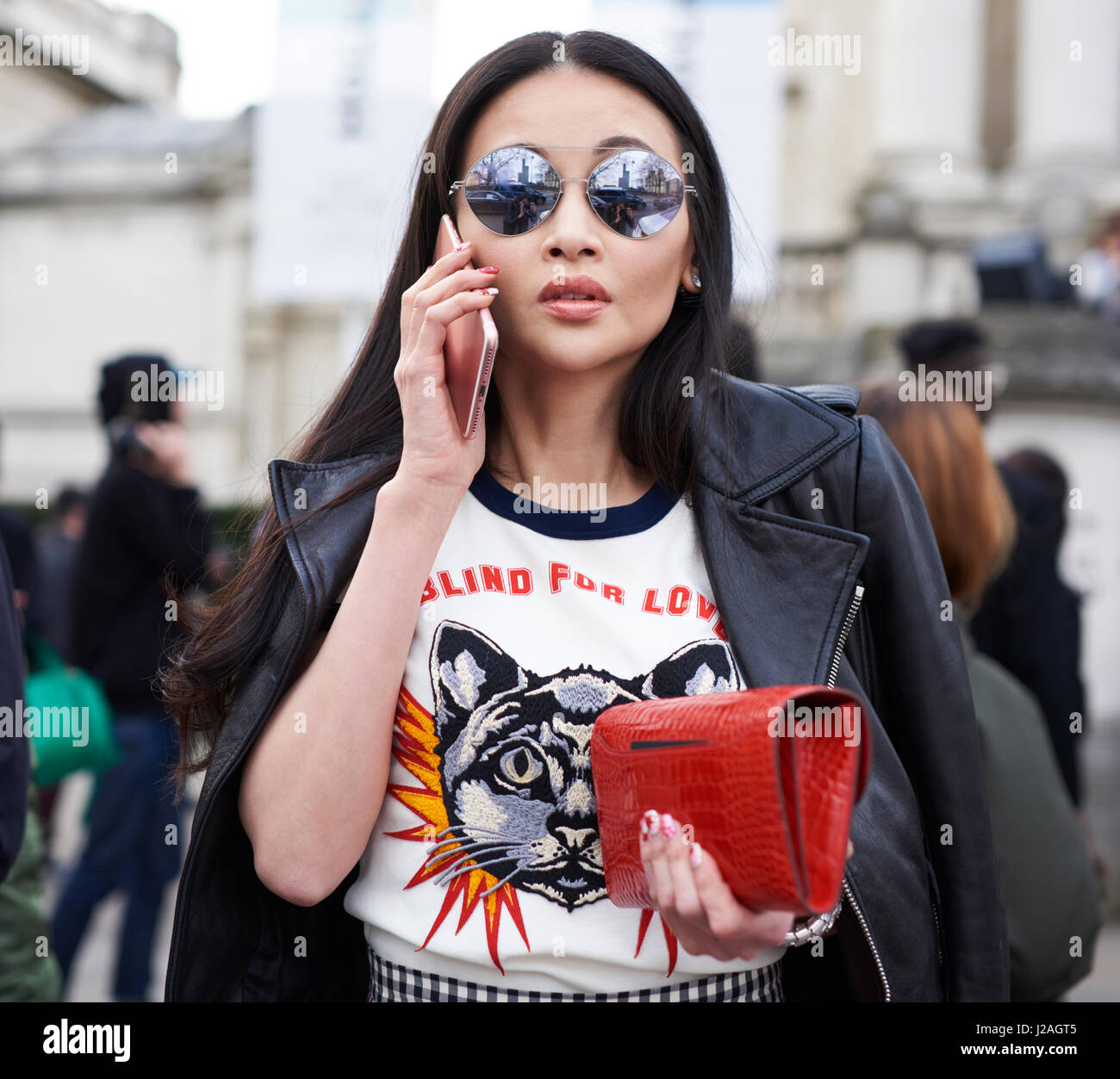 LONDON - FEBRUARY, 2017: Waist up view of woman wearing Gucci top and leather jacket, holding Hermes purse, using phone outside Christopher Kane fashion show, London Fashion Week, day four. Stock Photo