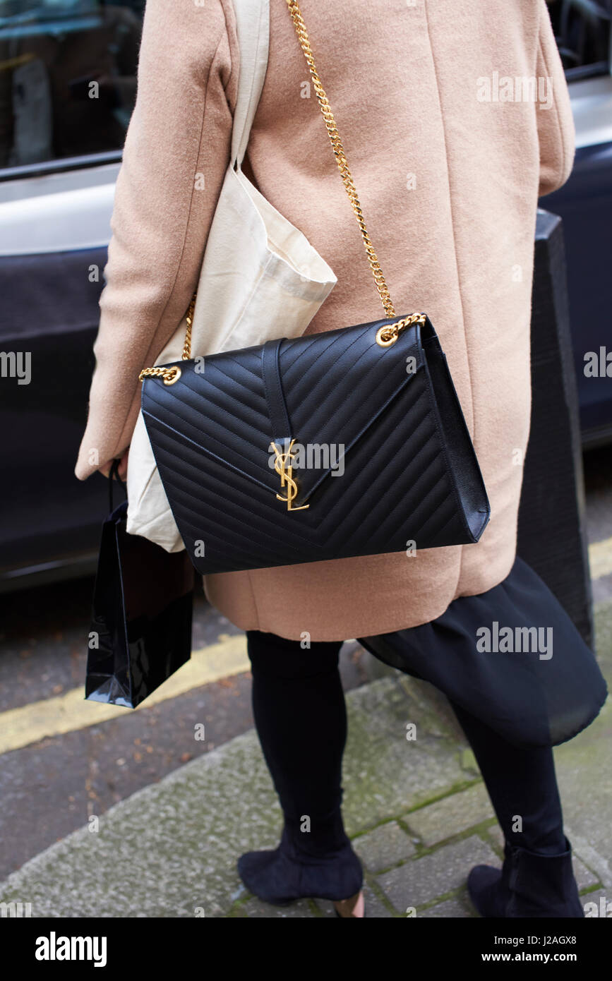 LONDON - FEBRUARY, 2017: Low section rear view of woman wearing a black Yves Saint Laurent cross body handbag standing in street, London Fashion Week, day five. Stock Photo