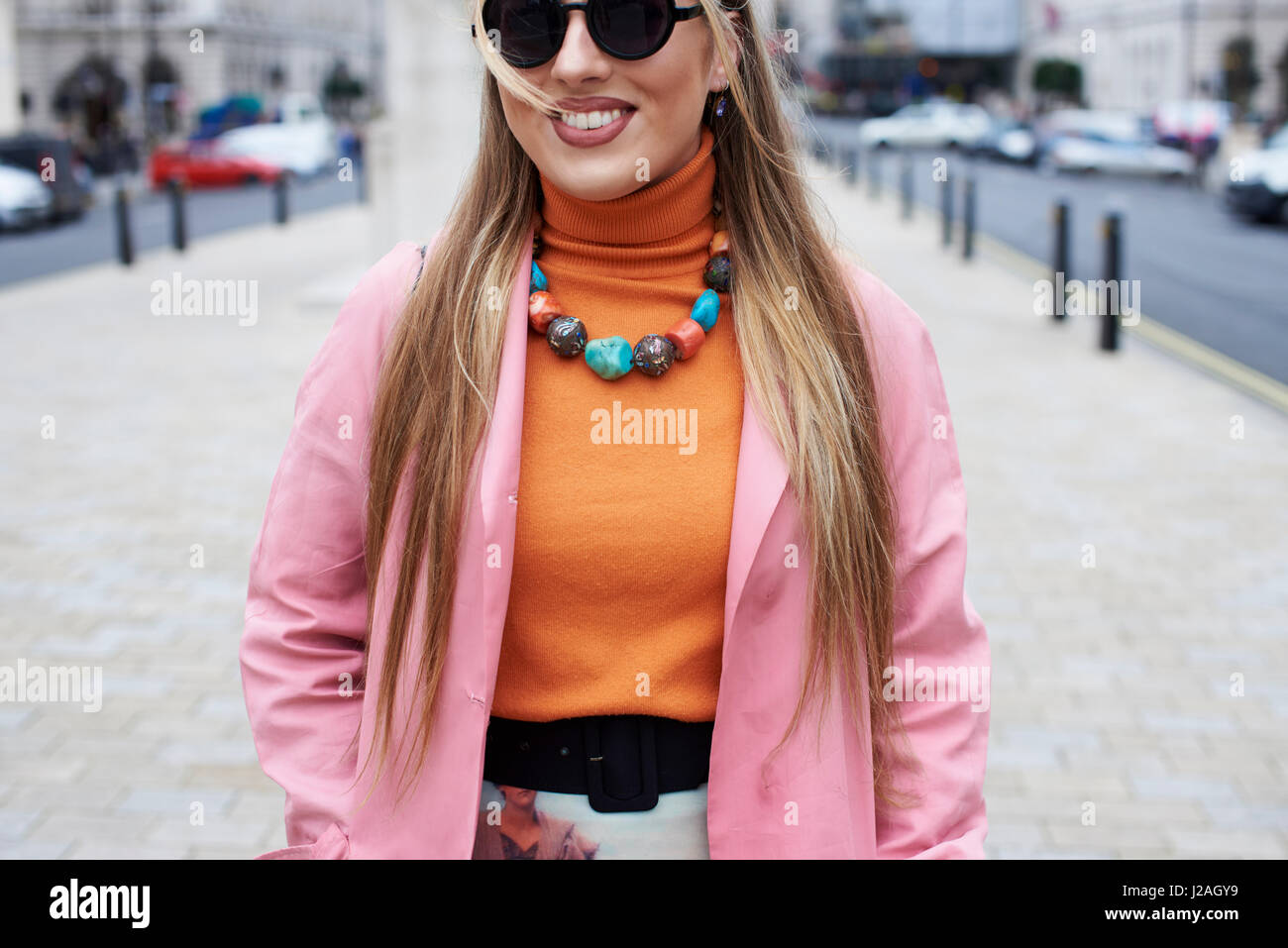 LONDON - FEBRUARY, 2017: Mid section of woman wearing pink coat and orange sweater with chunky stone necklace and rings standing in a street during London Fashion Week, day five. Stock Photo