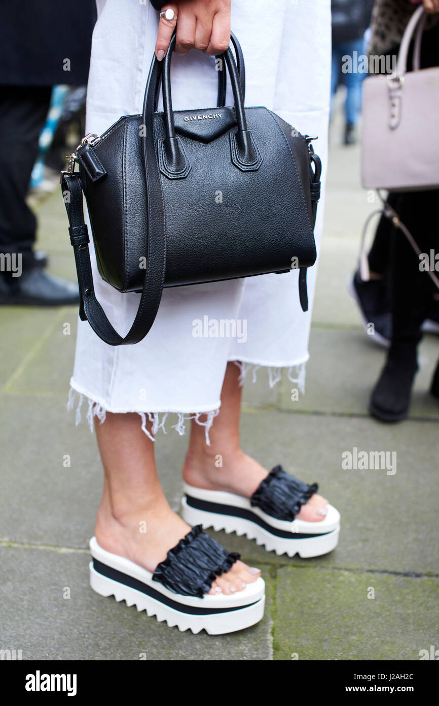 LONDON - FEBRUARY, 2017: Low section of woman wearing frayed cut-off trousers and wedge soled sandals holding black Givenchy Antigona tote bag in street during London Fashion Week, vertical Stock Photo