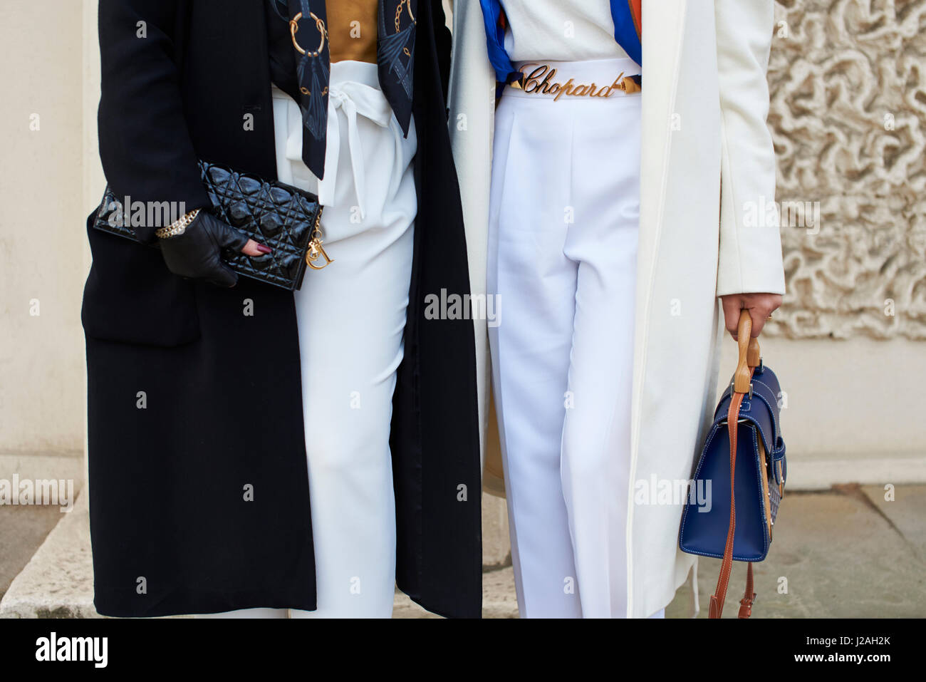 LONDON - FEBRUARY, 2017: Lower mid section of two women in the street holding handbags, a Chanel clutch bag on the left, while woman on the right wears a Chopard belt, during London Fashion Week, horizontal, front view Stock Photo