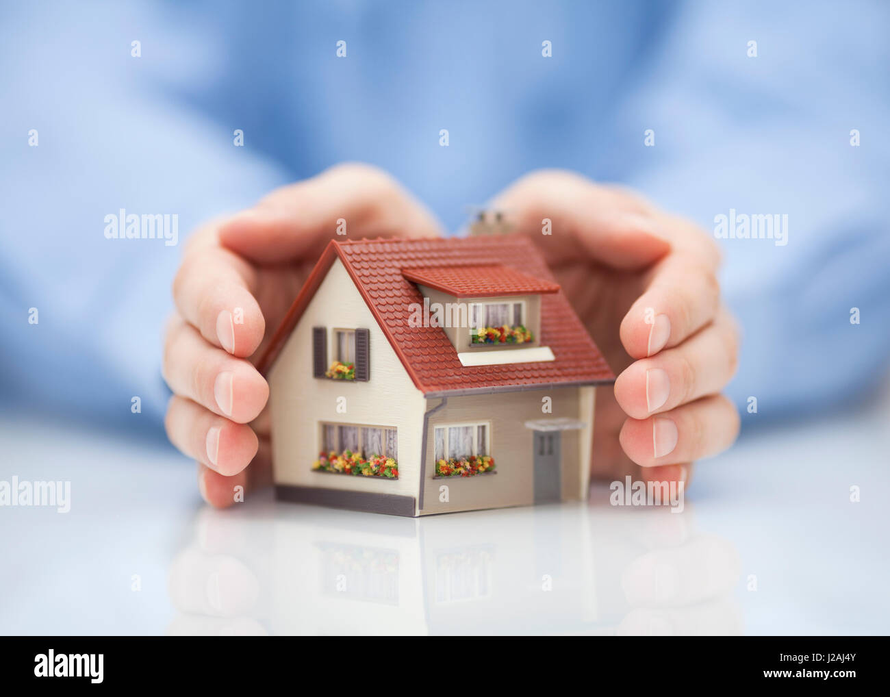Property insurance concept. Small toy house covered by hands Stock Photo
