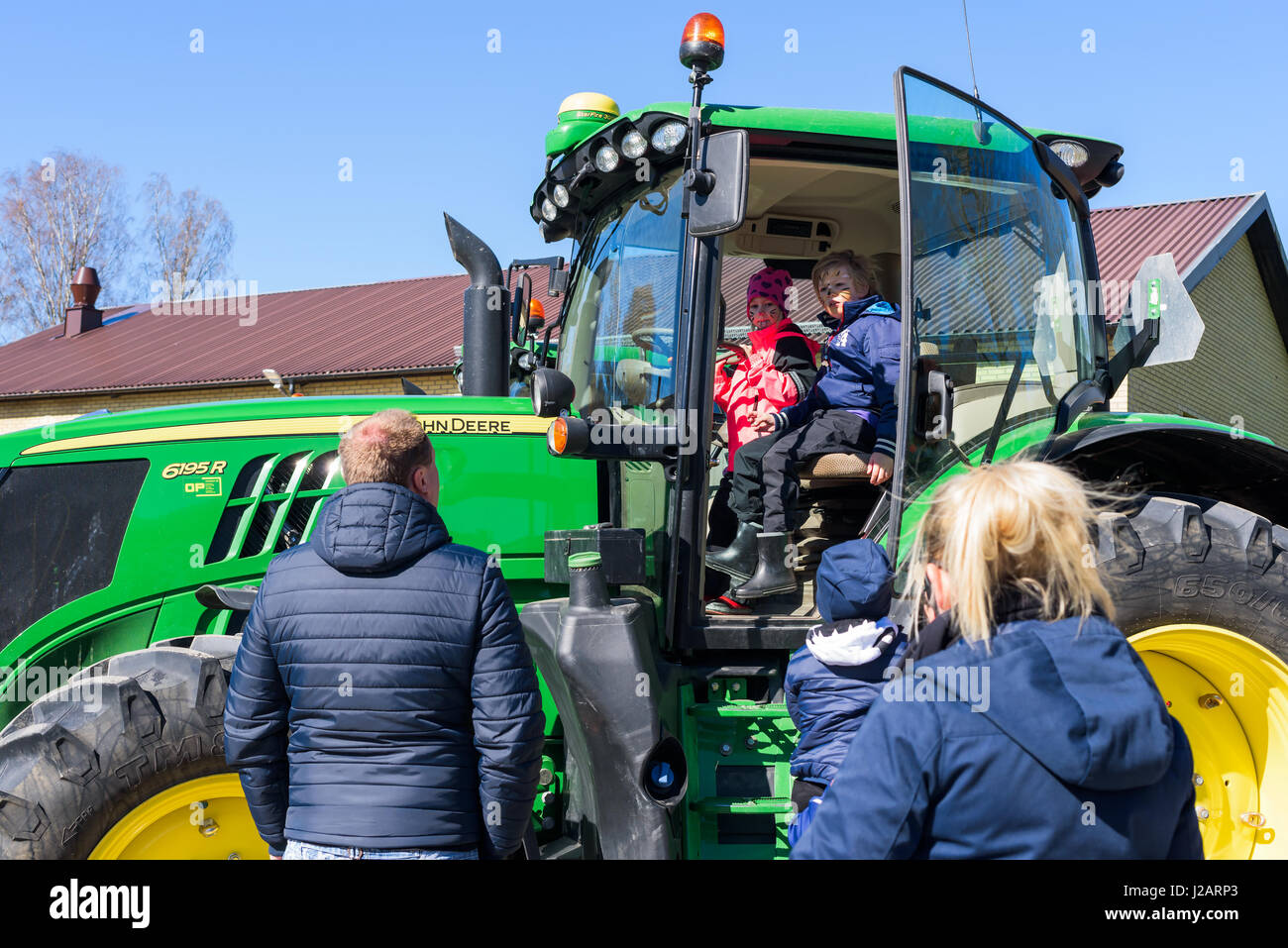 Brakne Hoby, Sweden - April 22, 2017: Documentary of small public farmers day. Children with painted faces sit inside a green John Deere tractor. Adul Stock Photo