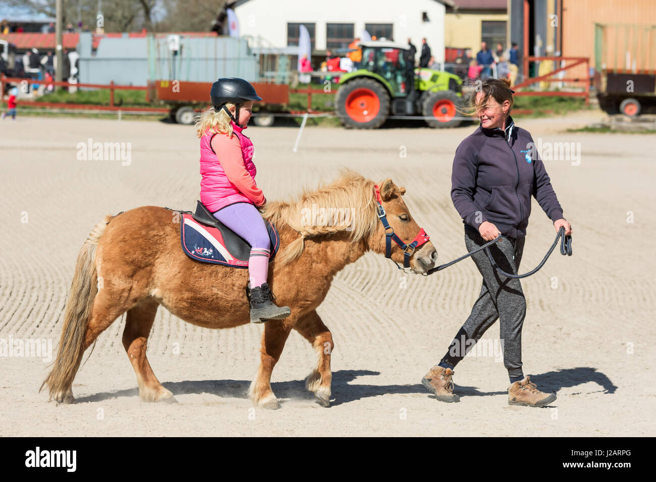 Brakne Hoby, Sweden - April 22, 2017: Documentary of small public farmers day. Young girl pony riding with adult handler in front of horse. Smiling fa Stock Photo