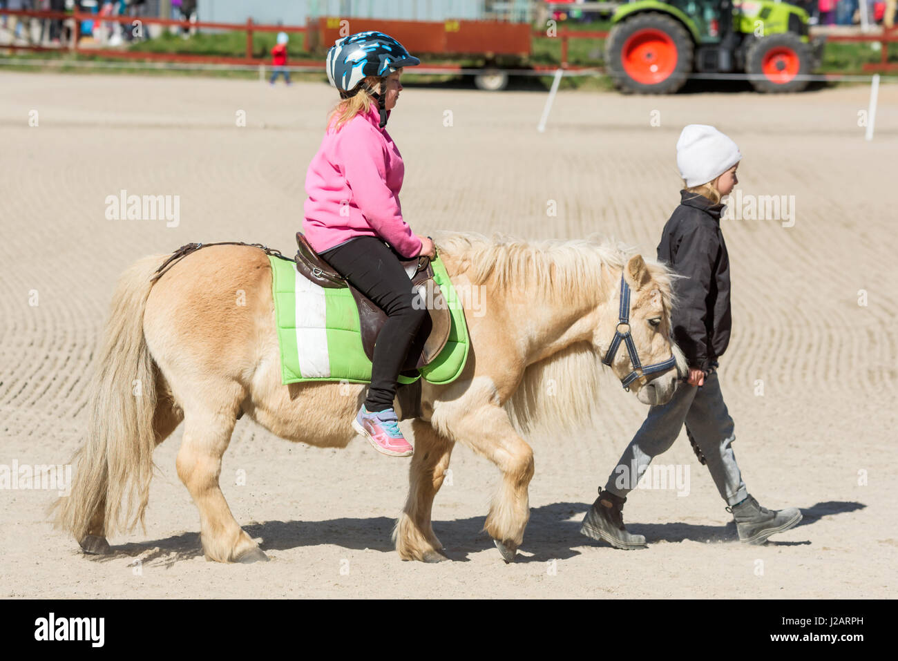 Brakne Hoby, Sweden - April 22, 2017: Documentary of small public farmers day. Young girl pony riding with young handler in front of horse. Both looki Stock Photo