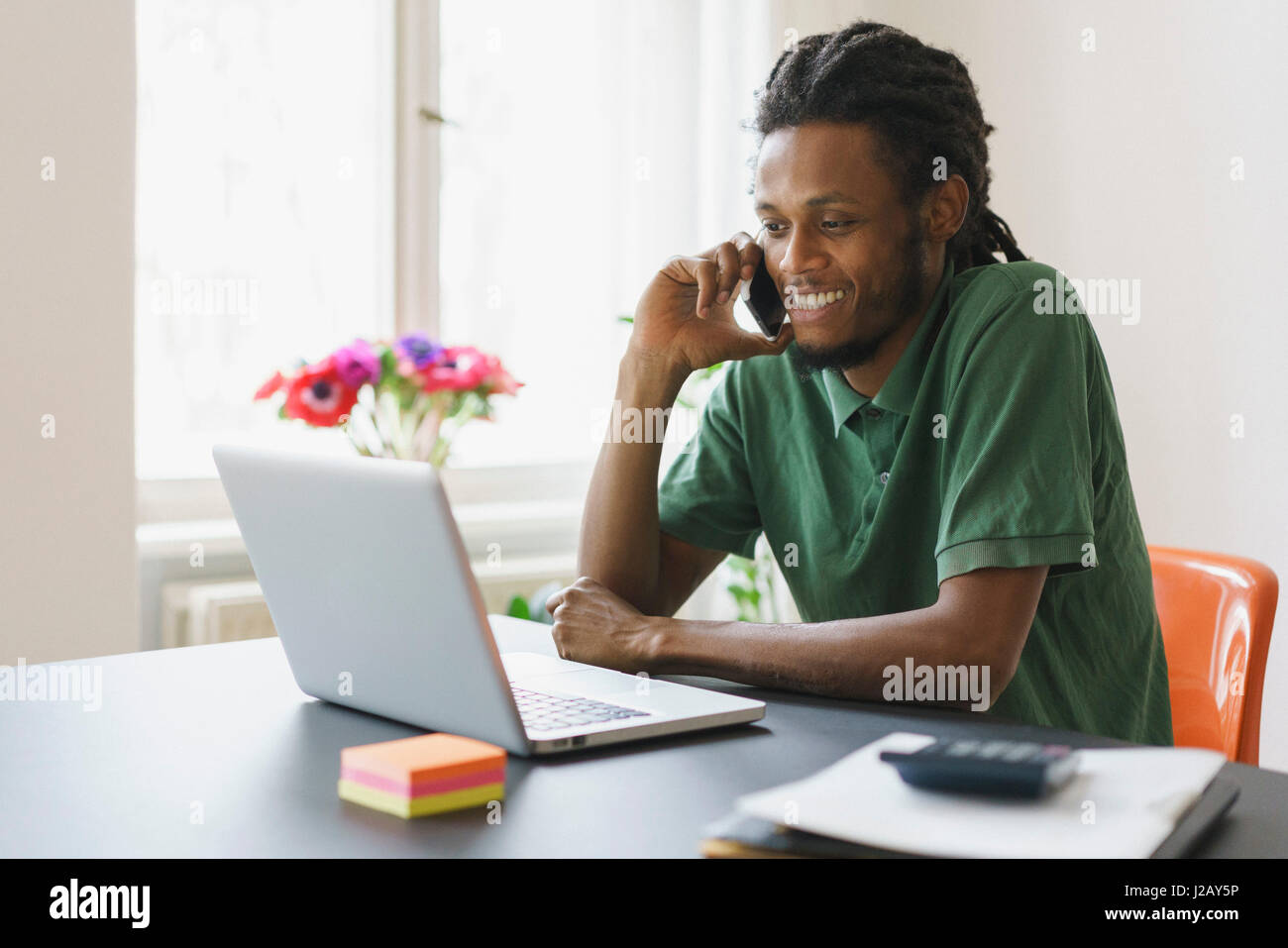 Happy man looking at laptop while using smart phone in house Stock Photo