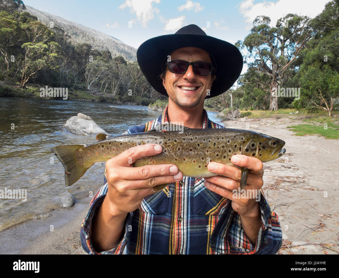 Portrait of happy mature man holding fish by river, Jindabyne, New South Wales, Australia Stock Photo