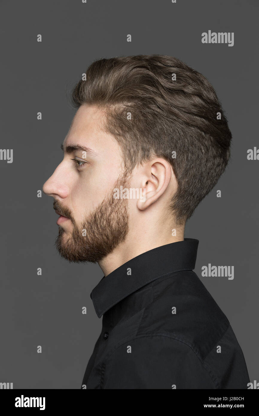 Side view of young man looking away against gray background Stock Photo