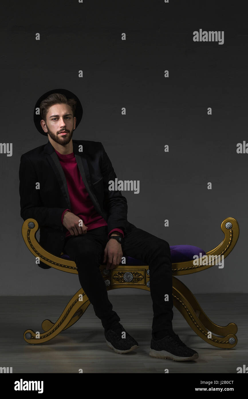 Portrait of confident man sitting on old-fashioned ottoman against gray background Stock Photo