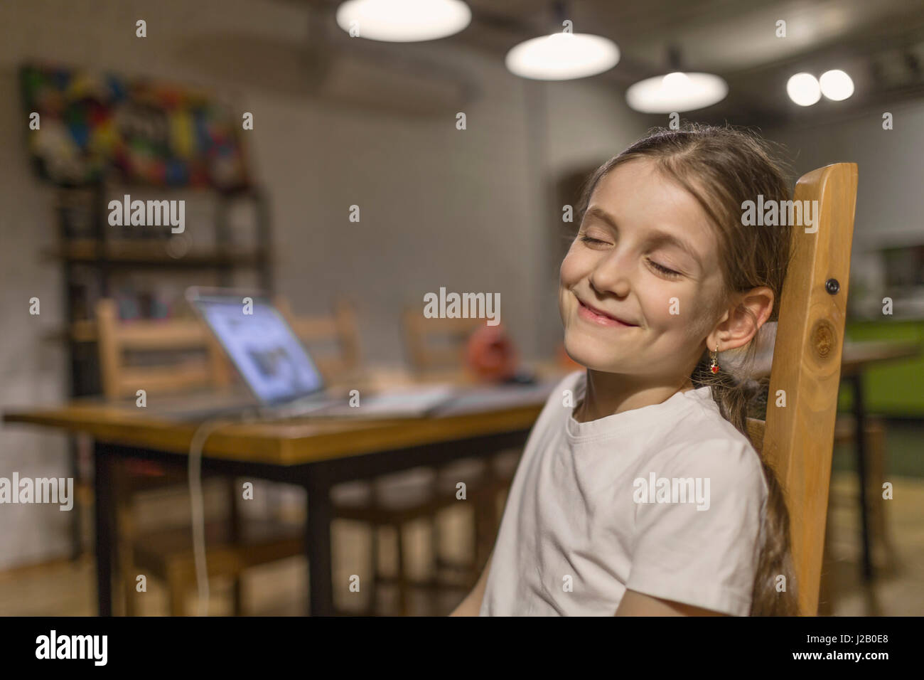 Portrait of smiling girl sitting with eyes closed on wooden chair at ...