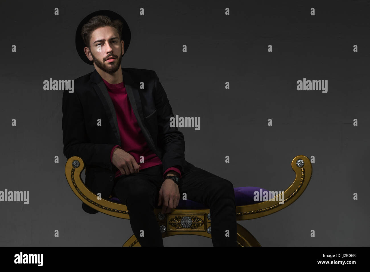 Portrait of confident man sitting on old-fashioned ottoman over gray background Stock Photo