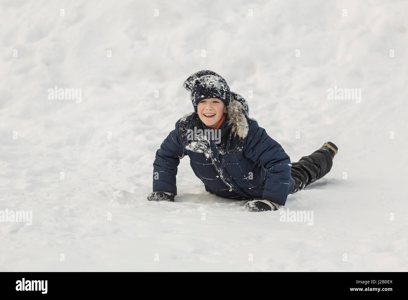 Cheerful boy looking away while lying in snow Stock Photo