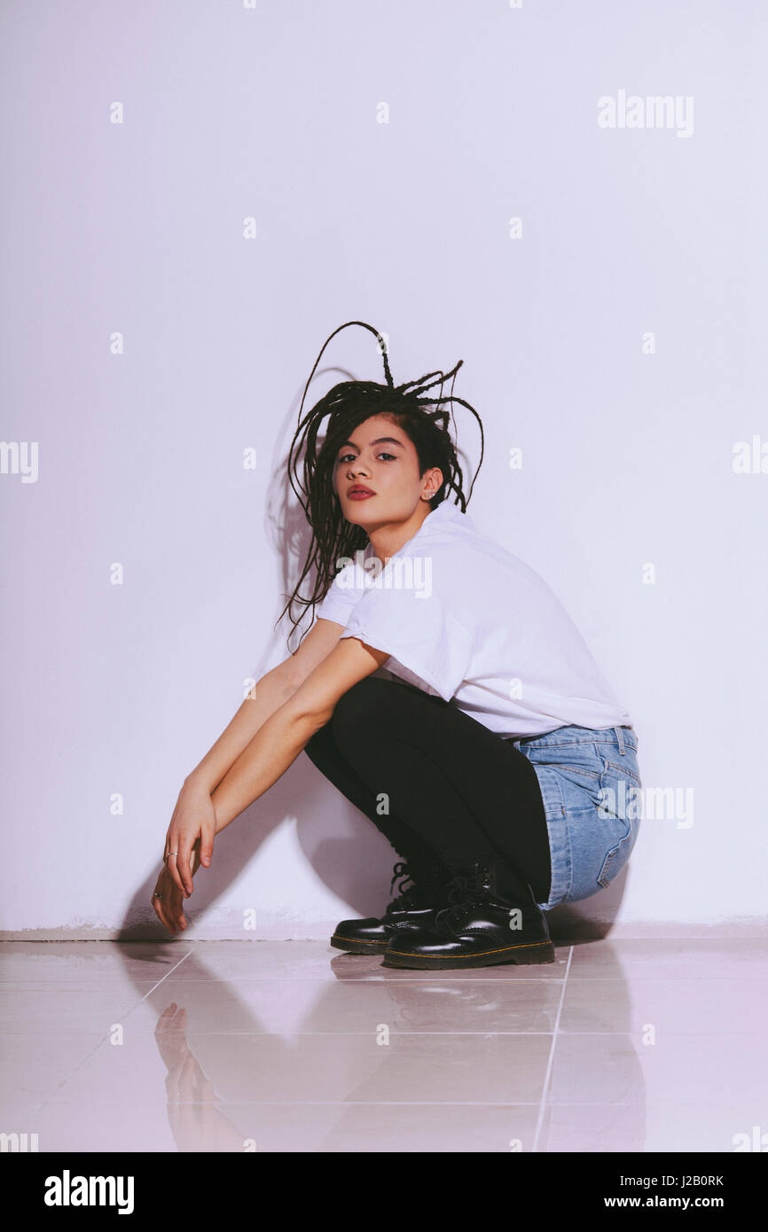 Portrait of fashion model crouching on tiled floor against white wall Stock Photo