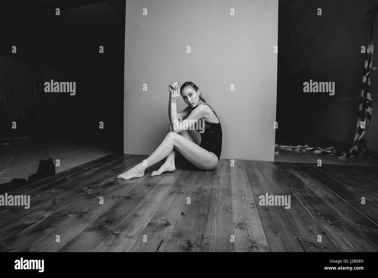 Portrait of fashion model sitting hardwood floor against wall Stock Photo