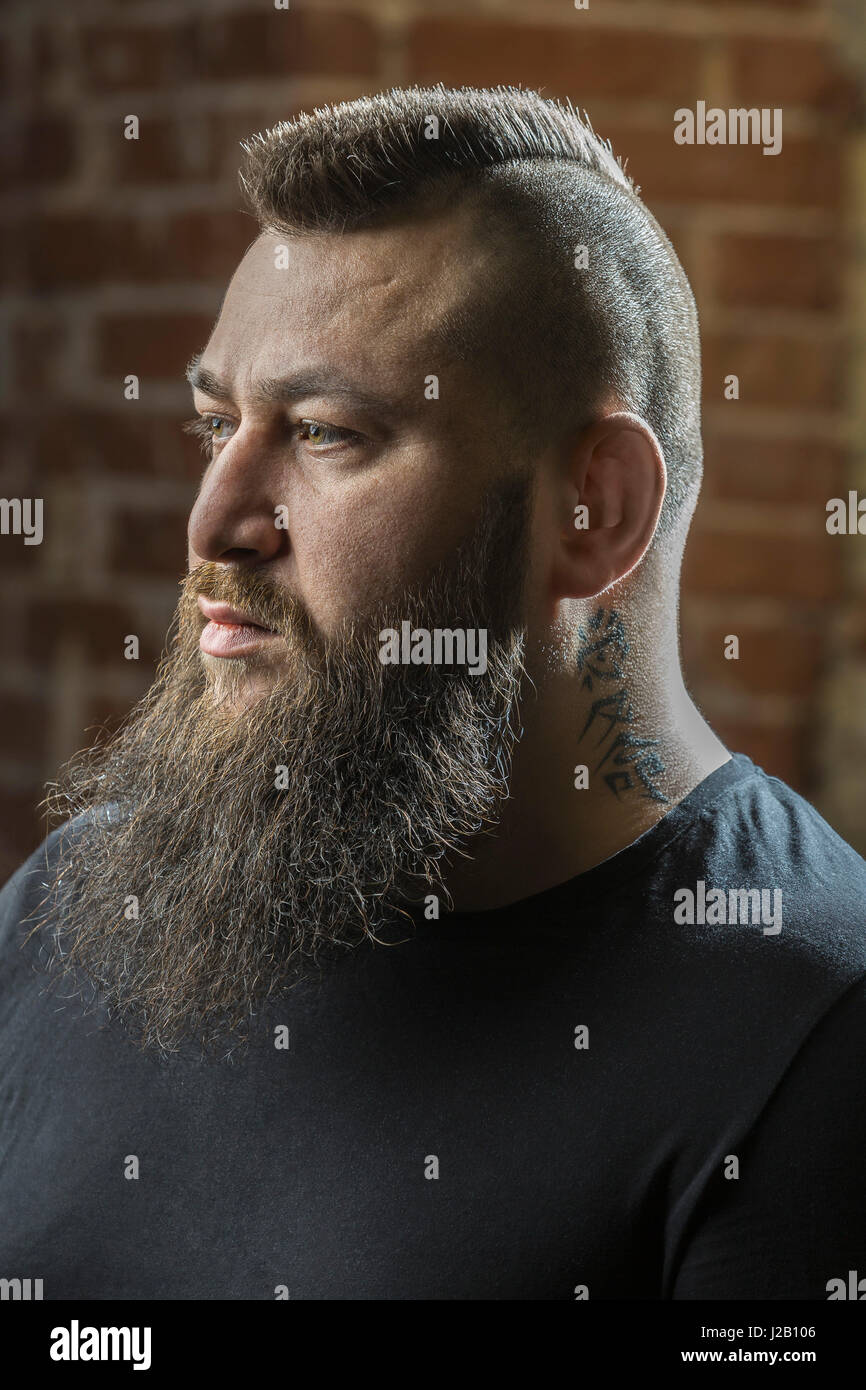Close-up of male hairdresser with beard and tattoo looking away at barber shop Stock Photo