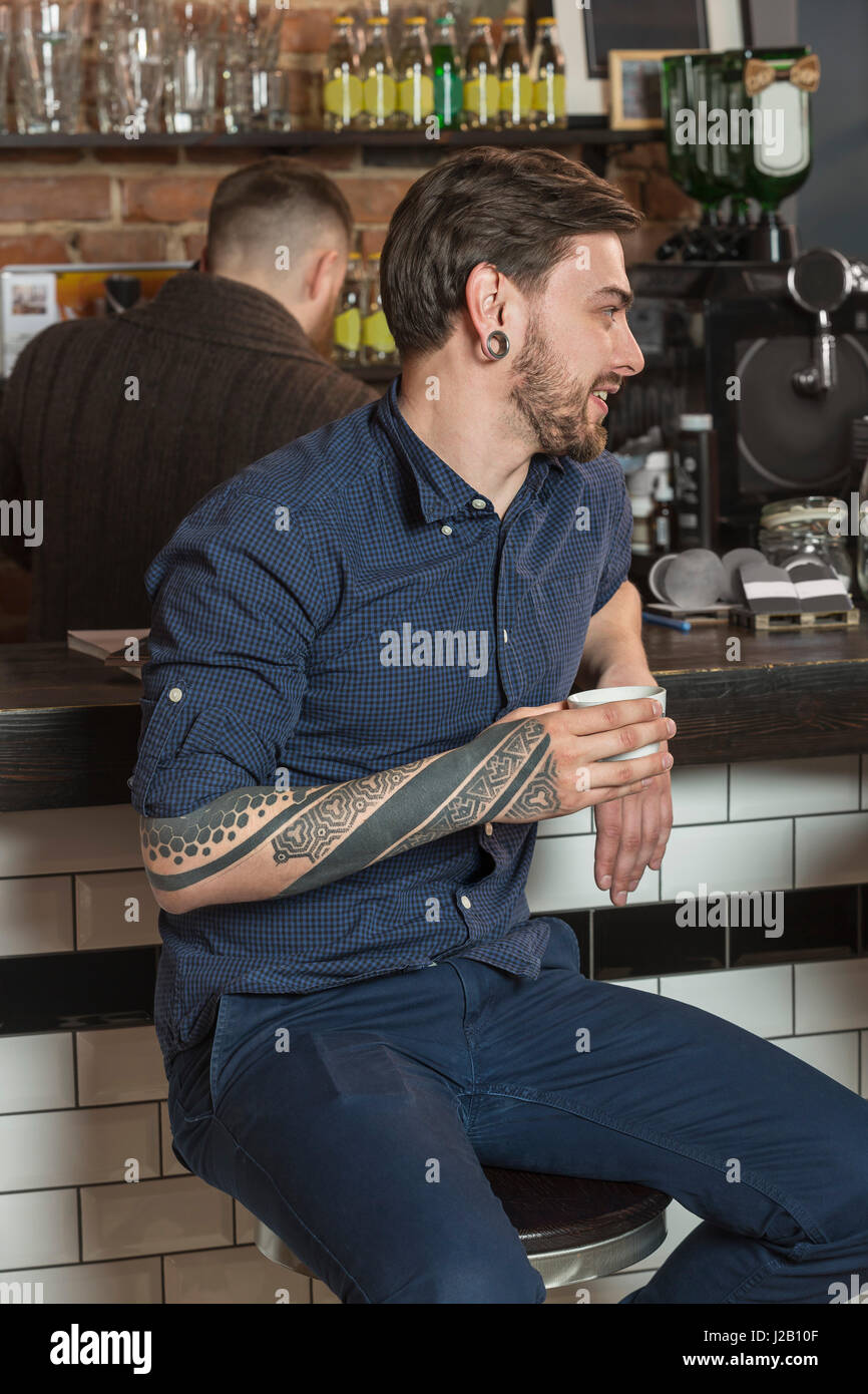 Happy hairdresser sitting with coffee at bar counter in barber shop Stock Photo