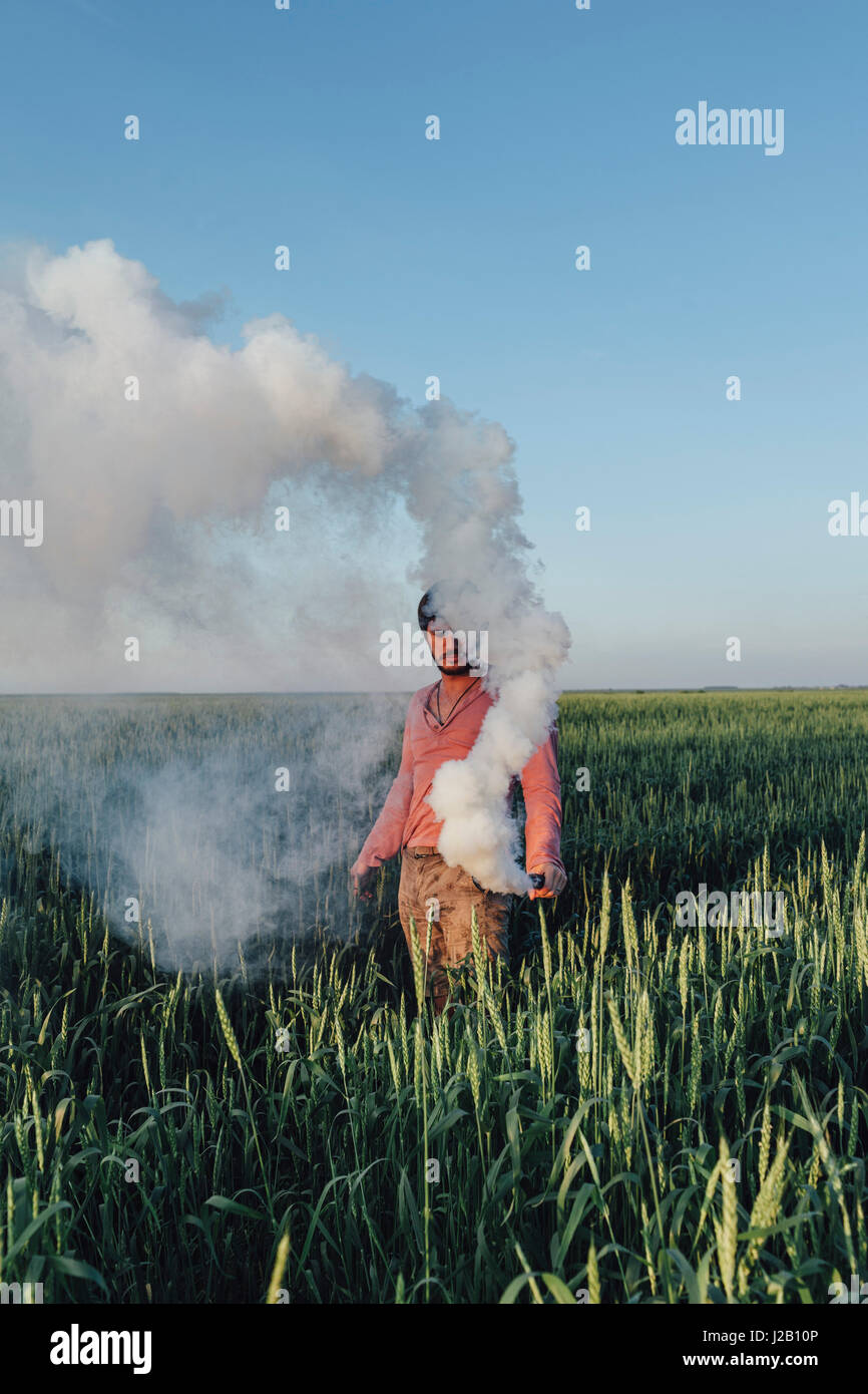 Man standing with distress flare emitting smoke on field against blue sky Stock Photo