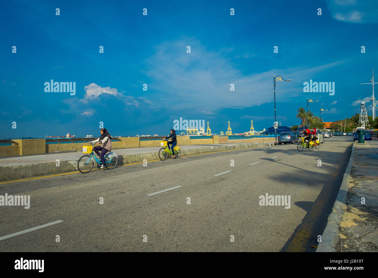 George Town, Malaysia - March 10, 2017: Beautiful scenic view of unknown muslim women riding bicycles along the Esplanade, a waterfront location in the heart of the city. Stock Photo