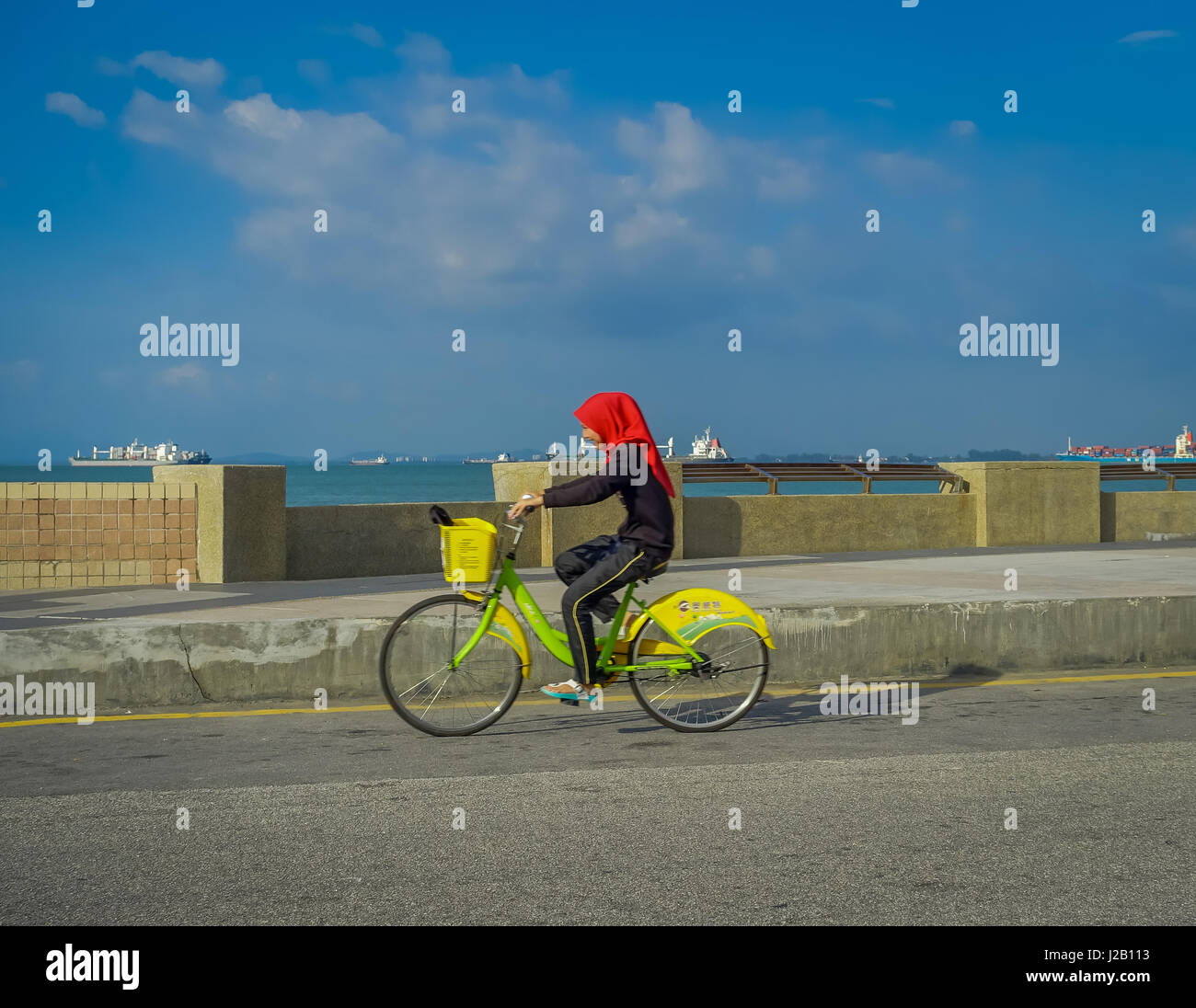 George Town, Malaysia - March 10, 2017: Beautiful scenic view of unknown muslim women riding bicycles along the Esplanade, a waterfront location in the heart of the city. Stock Photo