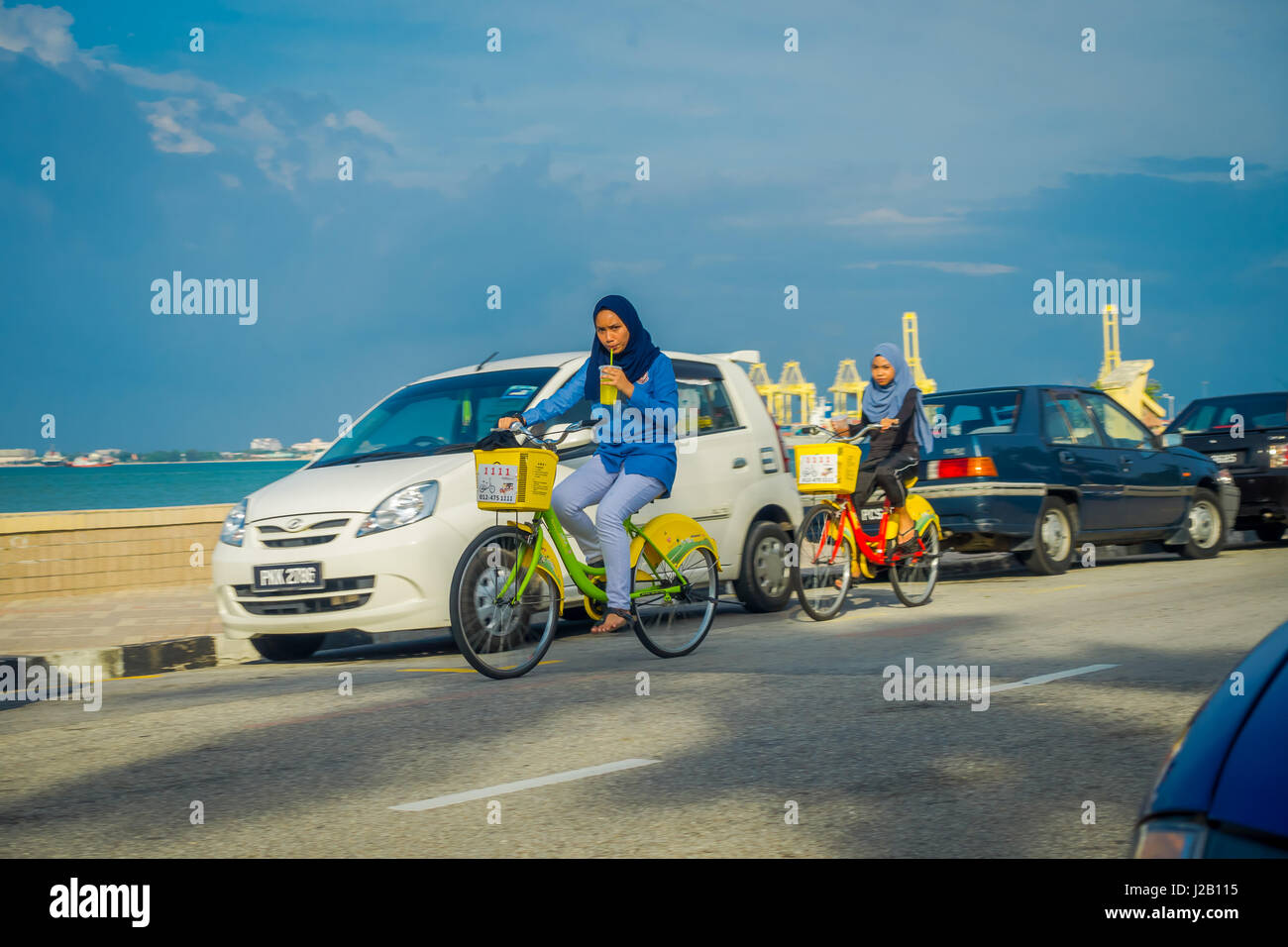 George Town, Malaysia - March 10, 2017: Beautiful scenic view of unknown muslim women riding bicycles along the Esplanade, a waterfront location in the heart of the city. Stock Photo
