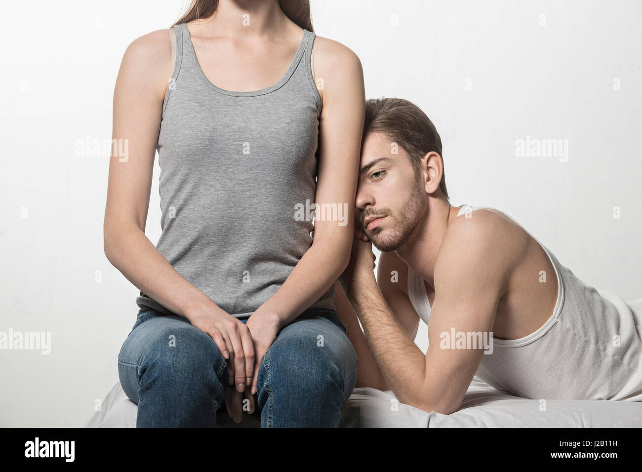 Thoughtful man leaning on girlfriend sitting at bed against white