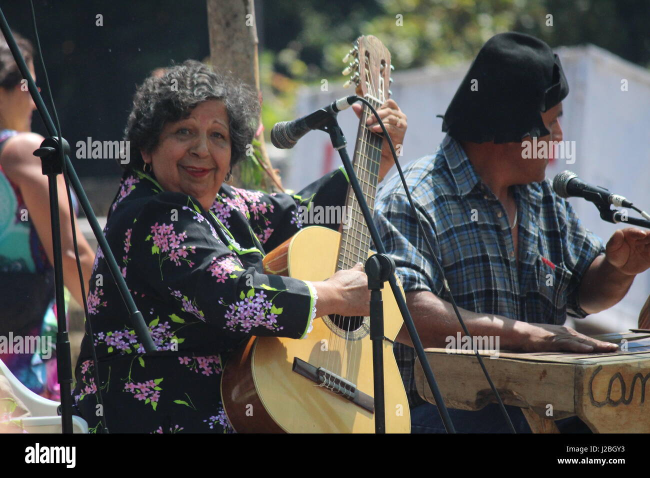 Plump lady in black flowery dress playing the guitar at local Festival in Chile looking at camera Stock Photo
