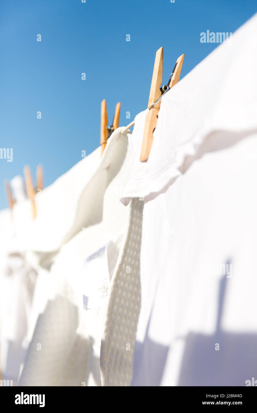 White clothes hung out to dry on a washing line in the bright warm sun. Background is a clear blue sky. Stock Photo