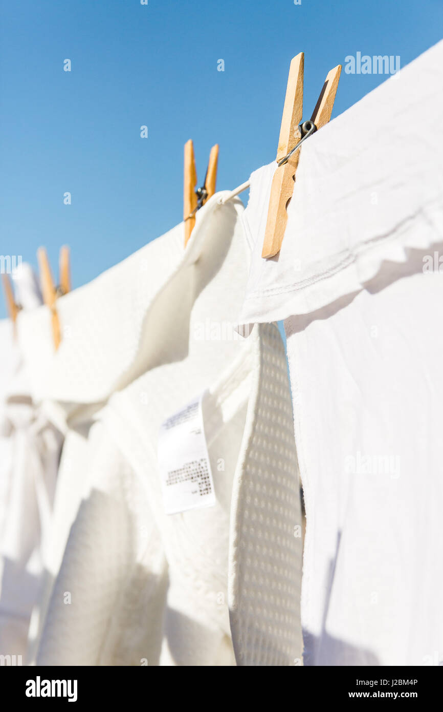 White clothes hung out to dry on a washing line in the bright warm sun. Background is a clear blue sky. Stock Photo