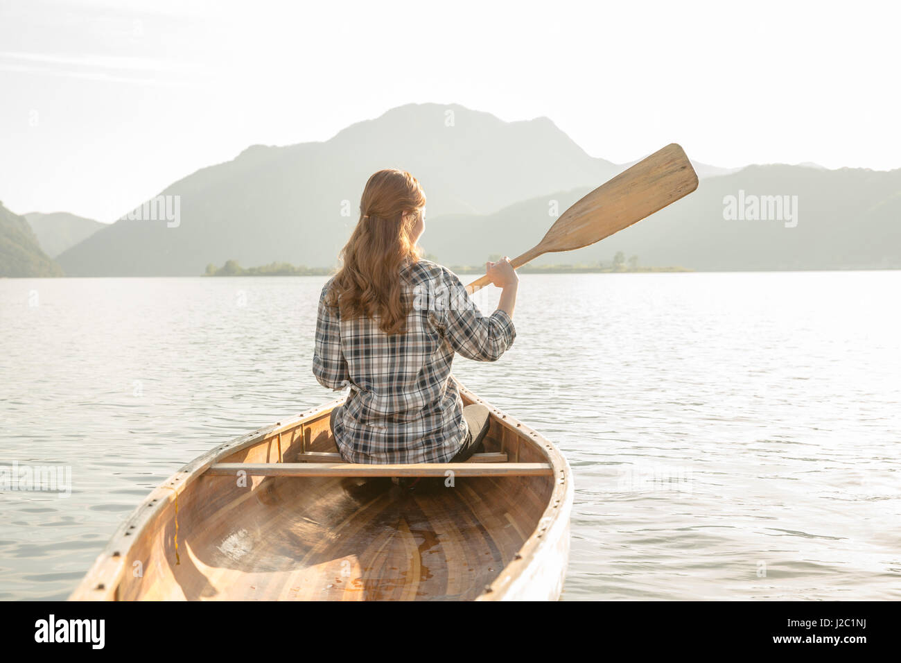 Back of female traveler paddling a canoe Stock Photo