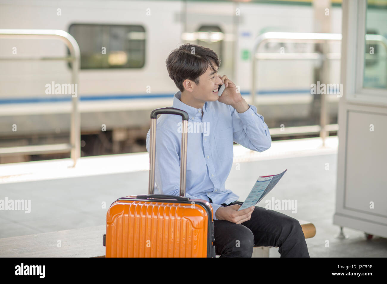Young man with carrier talking on cellphone at station Stock Photo