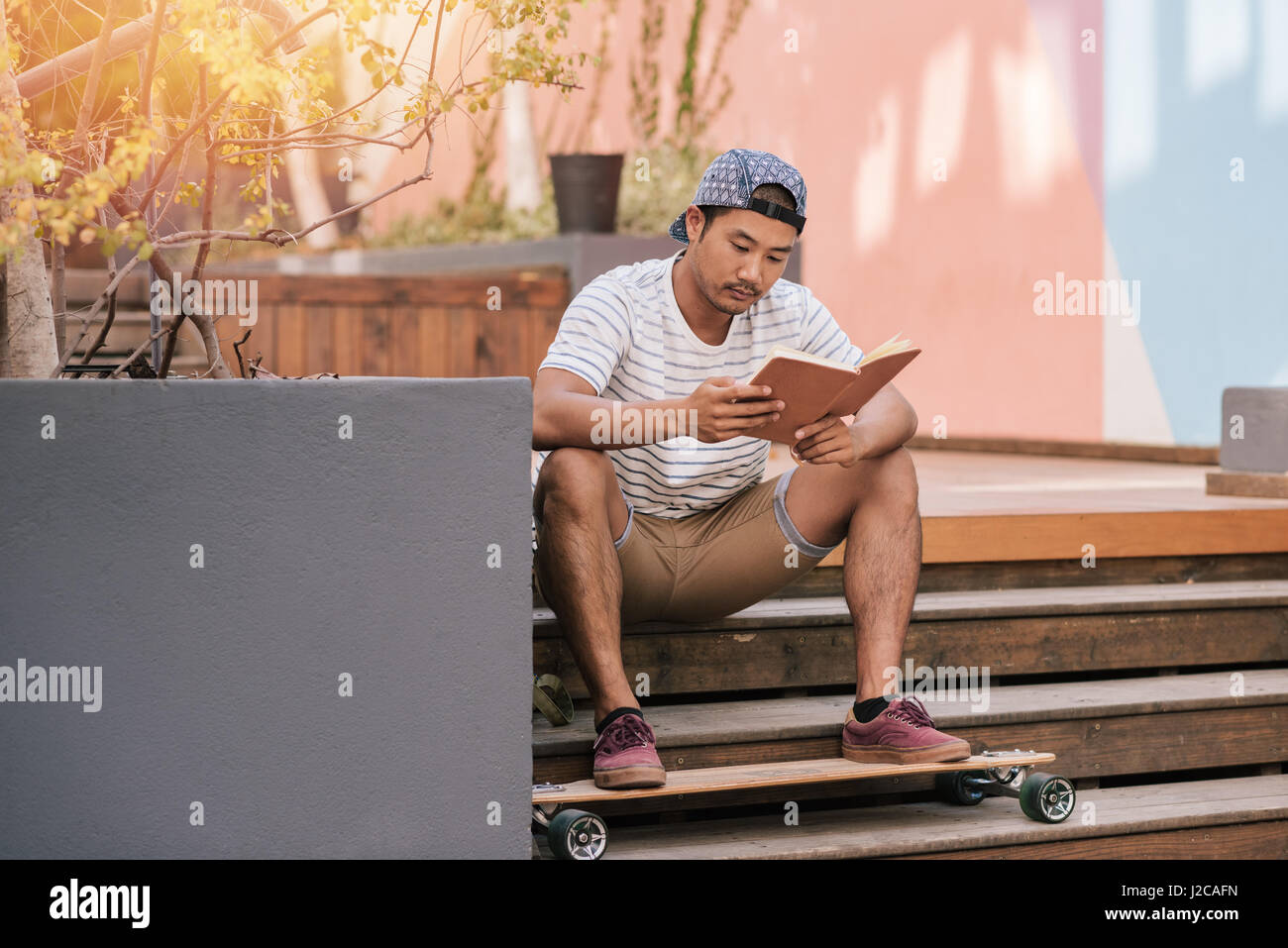 Young Asian man relaxing on stairs outside reading a book Stock Photo ...