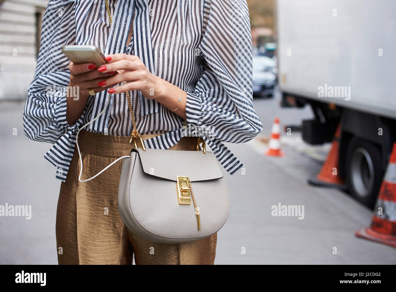 Mid section of woman in striped blouse using phone in street Stock Photo
