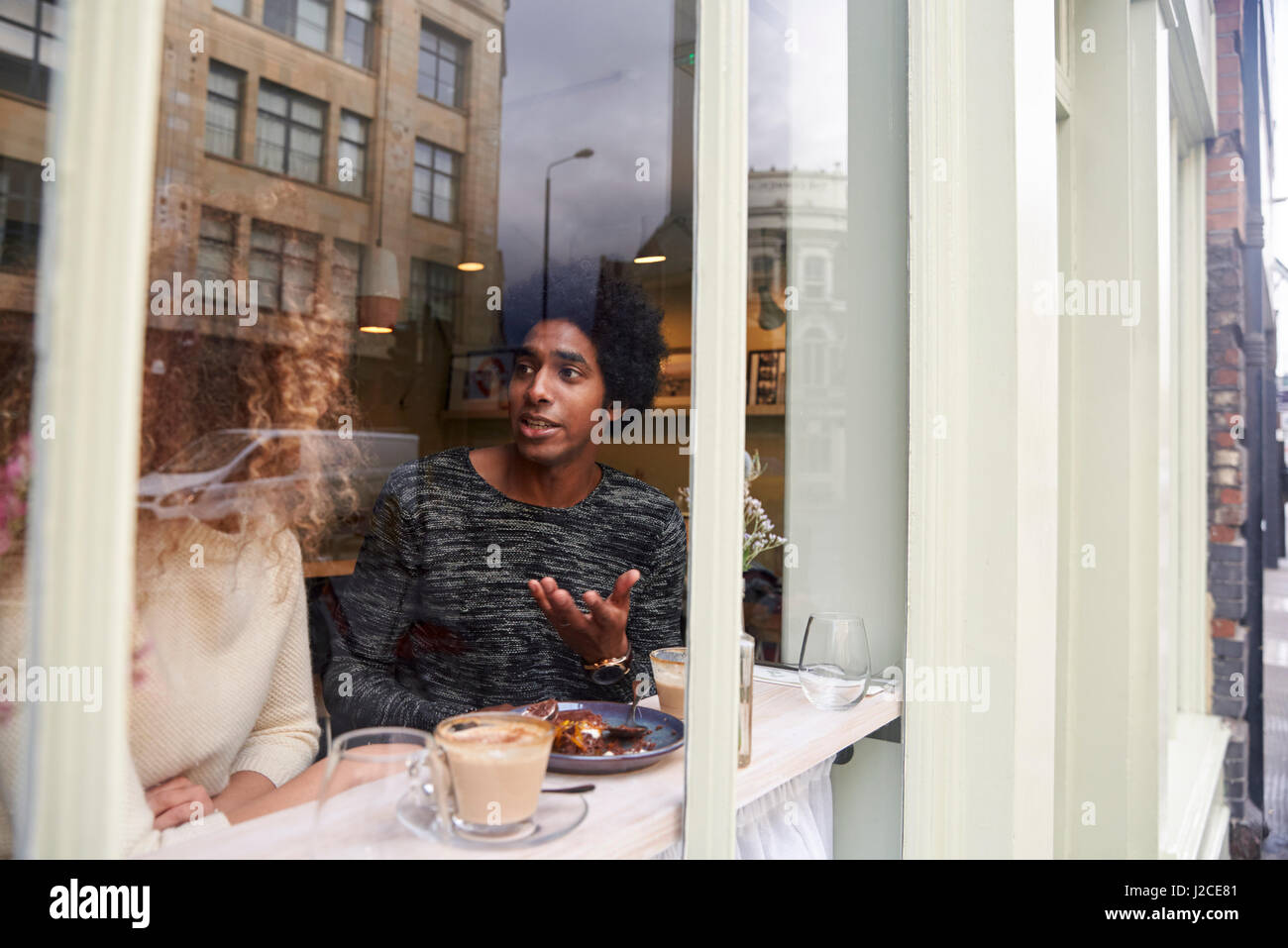 View Through Window Of Couple Enjoying Drink In Coffee Shop Stock Photo