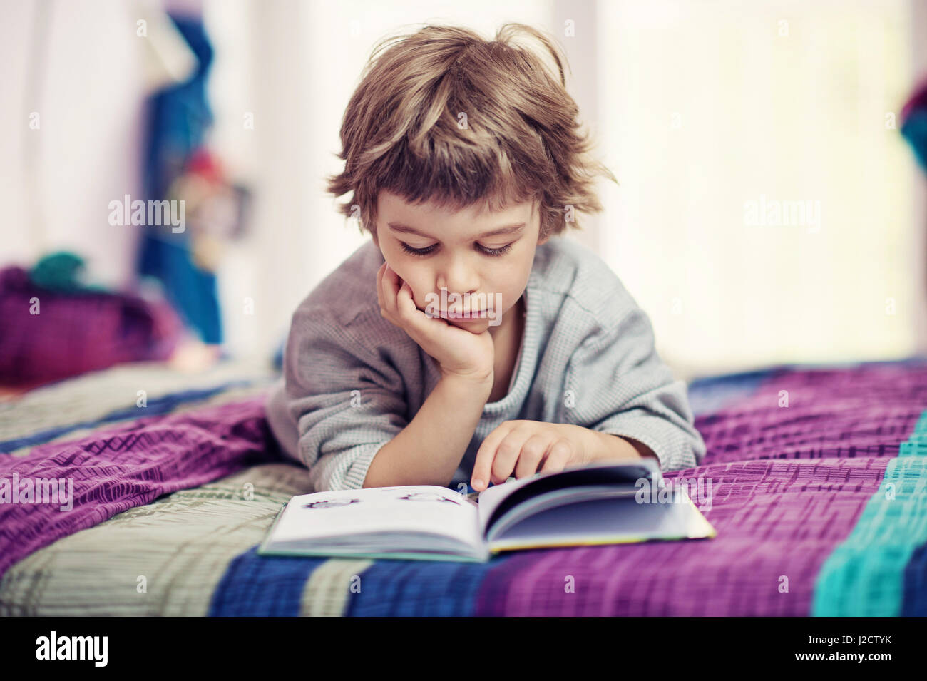 Cute little boy lying on bed reading book Stock Photo - Alamy