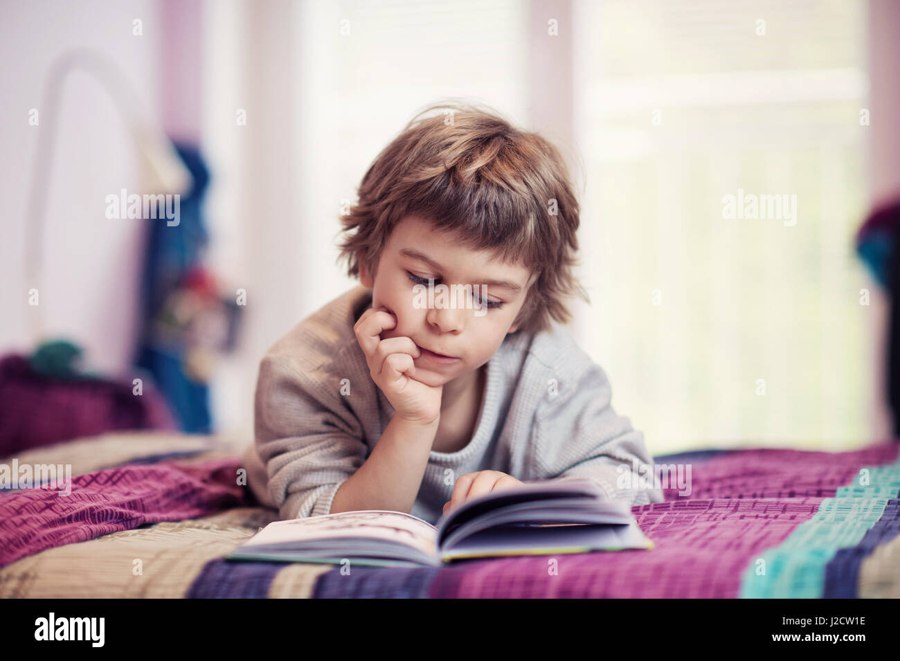 Cute little boy lying on bed reading book Stock Photo - Alamy