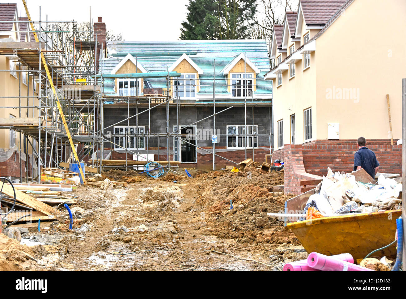 Mud clay winter building site small new uk housing property development site with one home painted scaffolding on two new houses roof on two homes Stock Photo