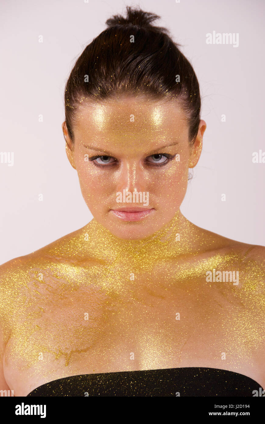 Beautiful brunette girl in the studio with gold paint sprayed on