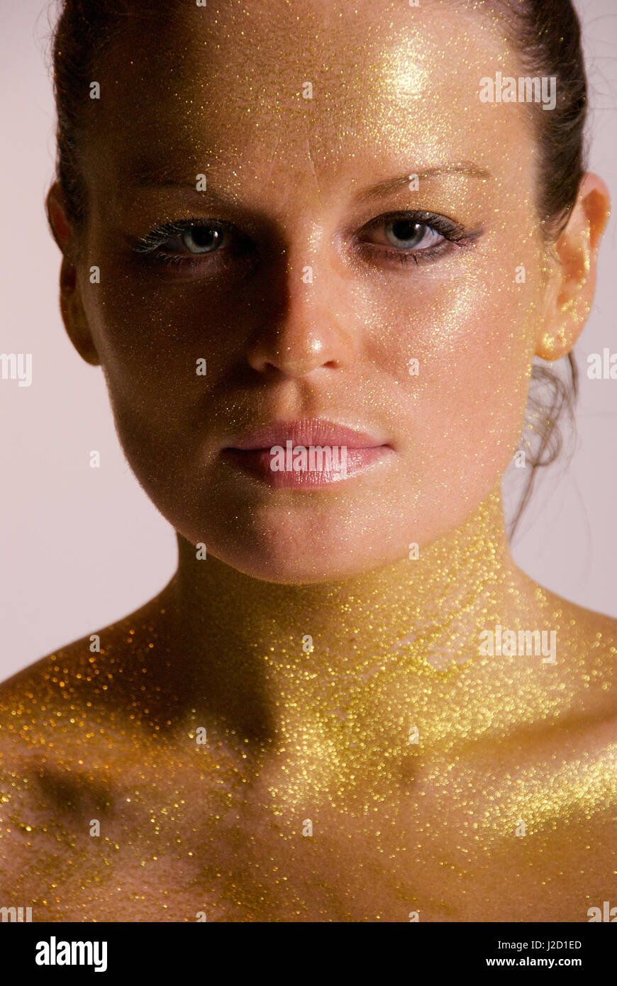 Beautiful brunette girl in the studio with gold paint sprayed on her body Stock Photo