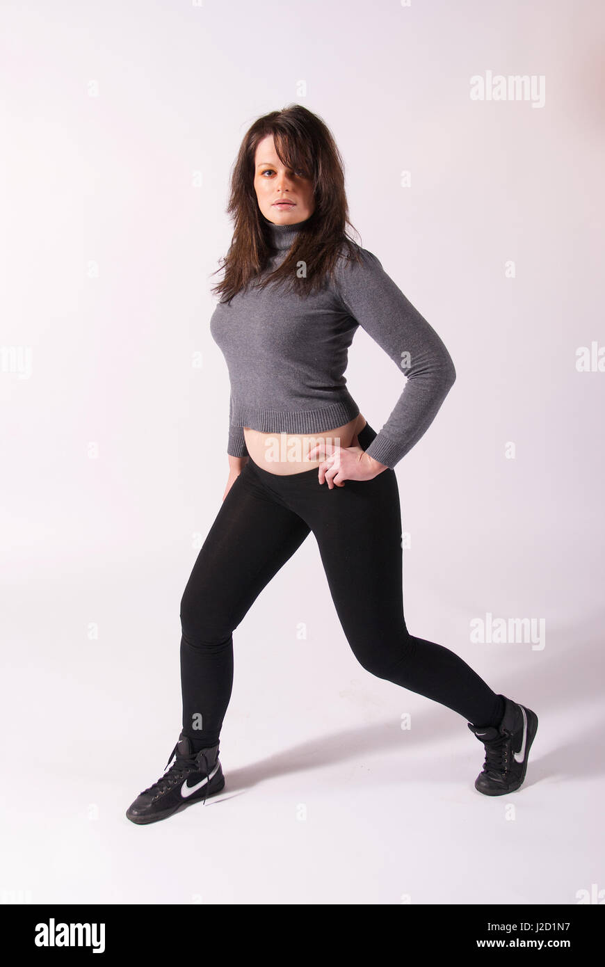 Beautiful brunette girl in the studio wearing black leggings and grey  jumper Stock Photo - Alamy