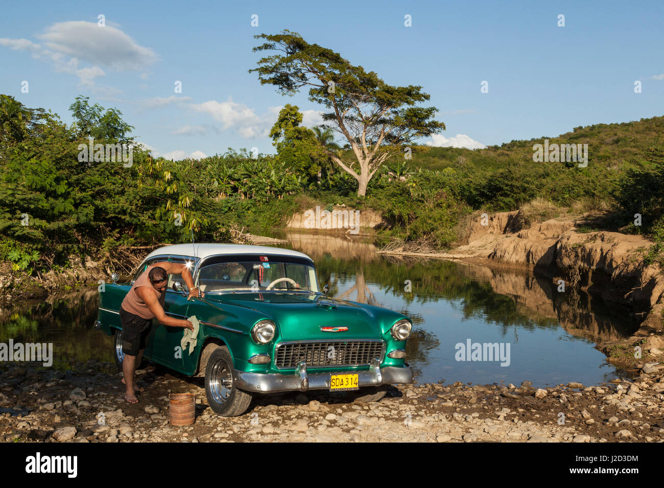 Cuba. A man washes his classic American car in the Gurabo river outside