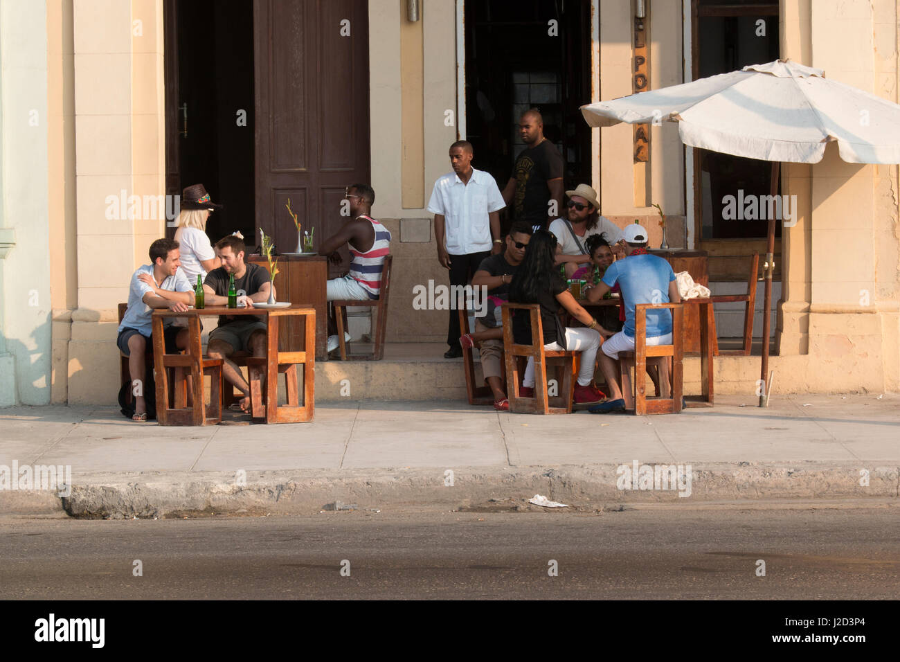 Havana Street scenes and Malecon promenade. Vintage cars, pedicabs and pedestrians share the route. Patrons at a cafe. (Editorial Use Only) Stock Photo