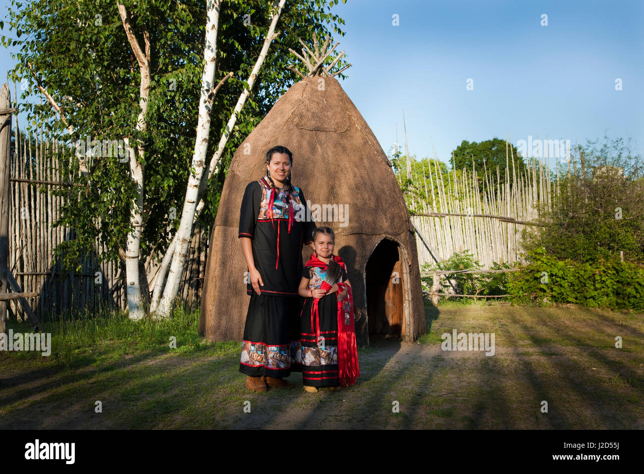 Ojibwe mother and daughter dressed in traditional ribbon dresses visit